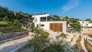 Une maison moderne à deux étages, dotée d’une piscine, entourée d’un jardin aménagé et d’un mur en pierre.