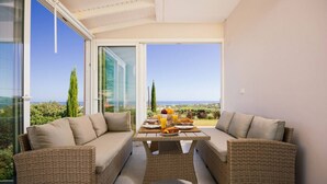Un balcón con mobiliario de mimbre y una mesa dispuesta para el desayuno, con vistas a un paisaje pintoresco.