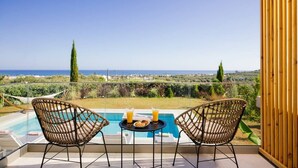 Un balcón con dos sillones de mimbre, una mesita con bebidas y aperitivos, y vista a la piscina.