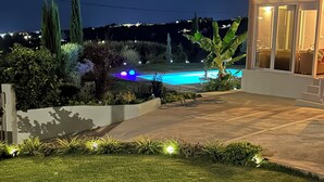 Vista nocturna de una propiedad residencial con piscina, césped cuidado y zona de patio.