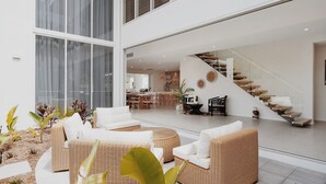 A spacious living area with wicker furniture, a staircase, and a kitchen in the background.