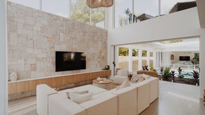 A modern living room with a stone wall, a flat-screen TV, a large beige sofa, and a view of the outdoors.