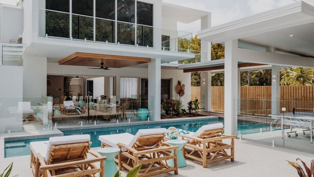 A modern outdoor pool area with wooden lounge chairs and a glass-enclosed patio.