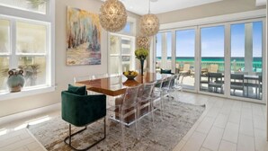 A spacious dining area with a wooden table, clear chairs, and a view of the ocean through large sliding doors.