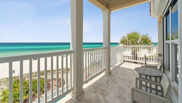 A covered balcony with a view of the ocean, white railings, and a small table and chair.