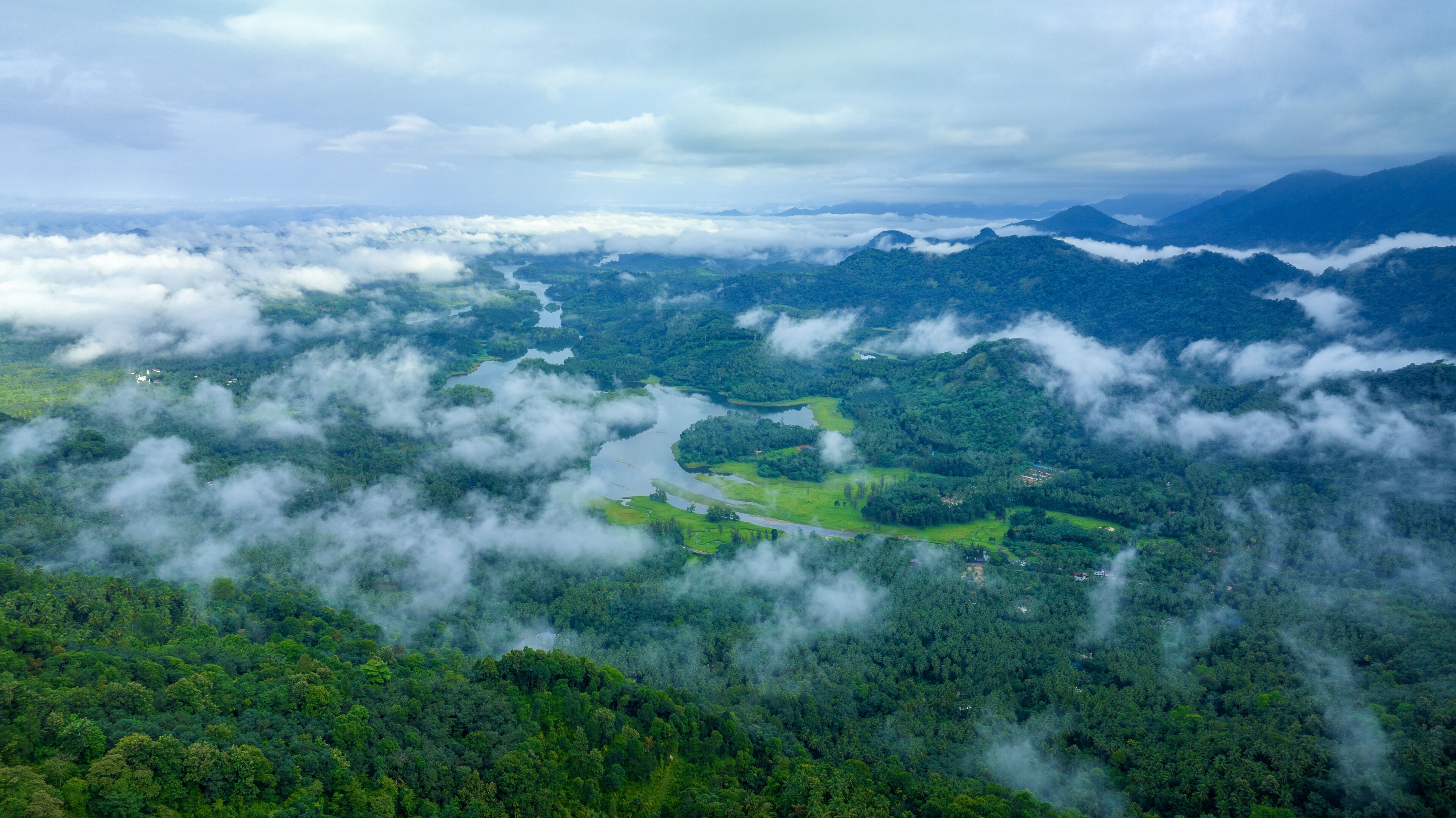 A lush green landscape with a river winding through it, surrounded by dense forest and mountains.