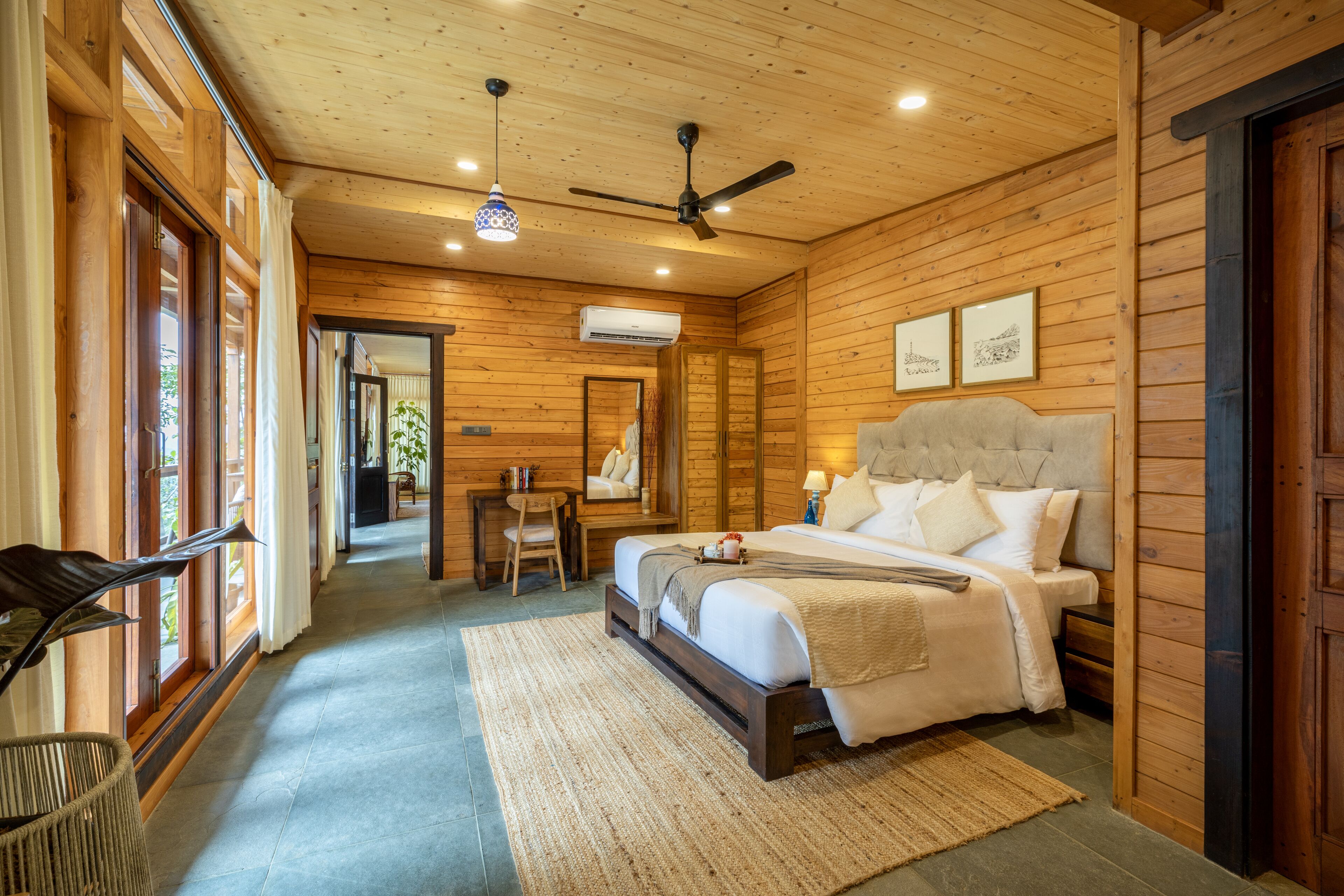 Un dormitorio de cabaña de madera con cama, ventilador de techo y una ventana grande.