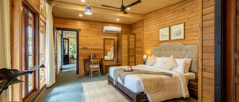 Un dormitorio de cabaña de madera con cama, ventilador de techo y una ventana grande.