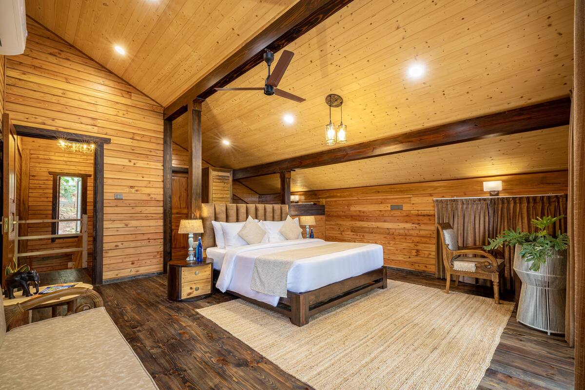 A wooden cabin-style bedroom with a bed, nightstands, a chair, and a ceiling fan.