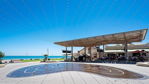 An outdoor plaza with a covered seating area, a fountain, and a view of the beach. - Vitamin Sea at Henley Beach (Henley Beach)