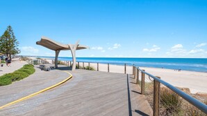 A wooden boardwalk leading to a beach with a concrete structure overhead. - Vitamin Sea at Henley Beach (Henley Beach)