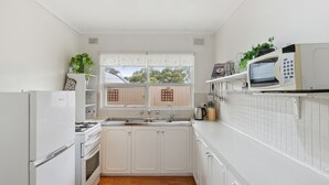 A compact kitchen with white cabinetry, a gas stove, a sink, and a microwave. - Vitamin Sea at Henley Beach (Henley Beach)