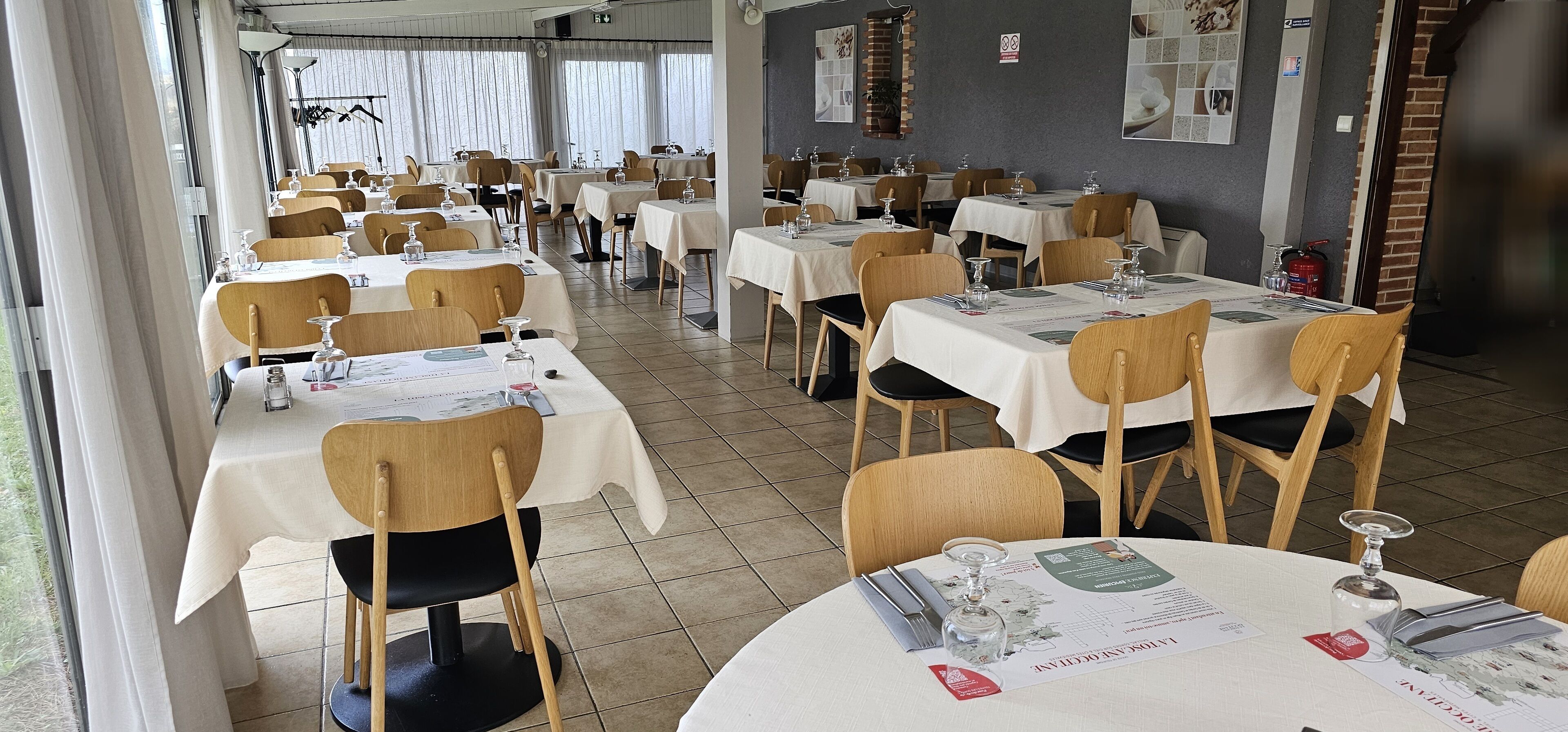 Un restaurante con varias mesas y sillas, cada conjunto con un menú, copas y cubiertos.