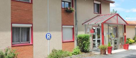 Un edificio con toldo rojo, entrada visible y señal de estacionamiento.