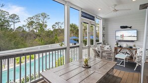 A covered outdoor area with a pool, wooden furniture, and a TV screen displaying a beach scene. - 6 Bikes & New 6-Seater Golf Cart, Blue Heron Haven Private Heated Pool! (Santa Rosa Beach)