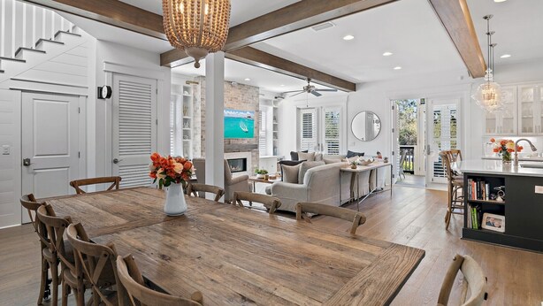 A spacious living area with a wooden dining table, comfortable seating, a large chandelier, and a view of a pool through the glass doors. - 6 Bikes & New 6-Seater Golf Cart, Blue Heron Haven Private Heated Pool! (Santa Rosa Beach)