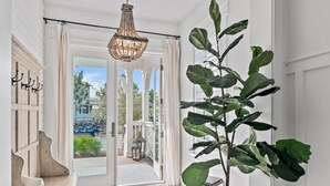 A bright hallway with a large potted plant, a chandelier, and a view of the outside. - Beaches Be Crazy FREE 6-Seater Golf Cart and 6 Bikes 2 Pools, Pickleball Courts at NatureWalk 30A! (Santa Rosa Beach)