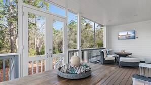 A covered outdoor deck with a wooden table, a round metal planter with driftwood, and a wicker sofa with cushions. - Beaches Be Crazy FREE 6-Seater Golf Cart and 6 Bikes 2 Pools, Pickleball Courts at NatureWalk 30A! (Santa Rosa Beach)
