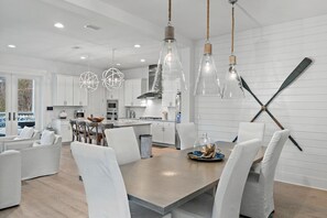 Une cuisine moderne avec des meubles blancs, un coin repas avec des chaises blanches et des luminaires suspendus.
