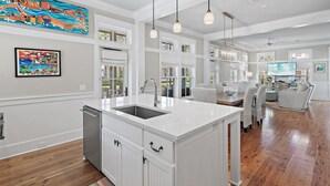 Una cocina amplia con una isla grande, muebles blancos e iluminación colgante.