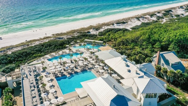 Vista aérea de un resort con varias piscinas, una playa y abundante vegetación.