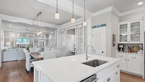 Una cocina moderna con armarios blancos, una isla grande con fregadero e iluminación colgante.