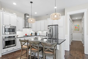 A modern kitchen with white cabinetry, stainless steel appliances, and a central island with bar stools. - Barefoot Bliss at Nature Walk Heated Resort Pools Pickleball Courts 6 Bikes, 6 Seater Golf Cart (Santa Rosa Beach)