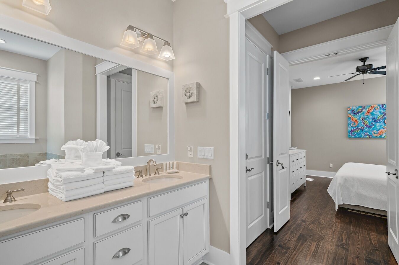 A modern bathroom with a large mirror, a sink with a towel stack, and a ceiling fan.