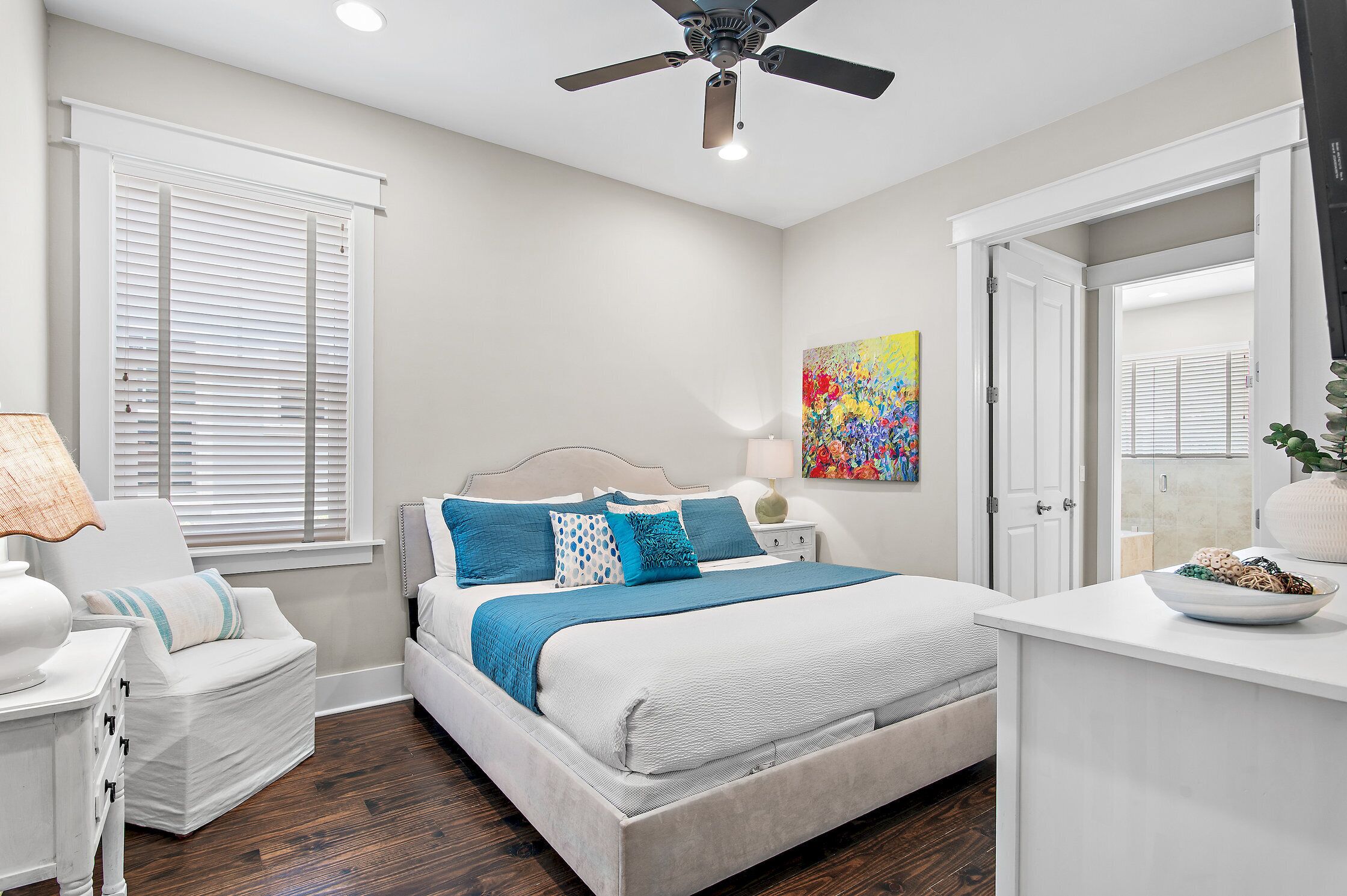A bedroom with a bed, a chair, a nightstand, a ceiling fan, a window with blinds, and a door.