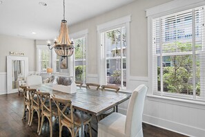 A dining area with a wooden table, chairs, and a chandelier. - Barefoot Bliss at Nature Walk Heated Resort Pools Pickleball Courts 6 Bikes, 6 Seater Golf Cart (Santa Rosa Beach)