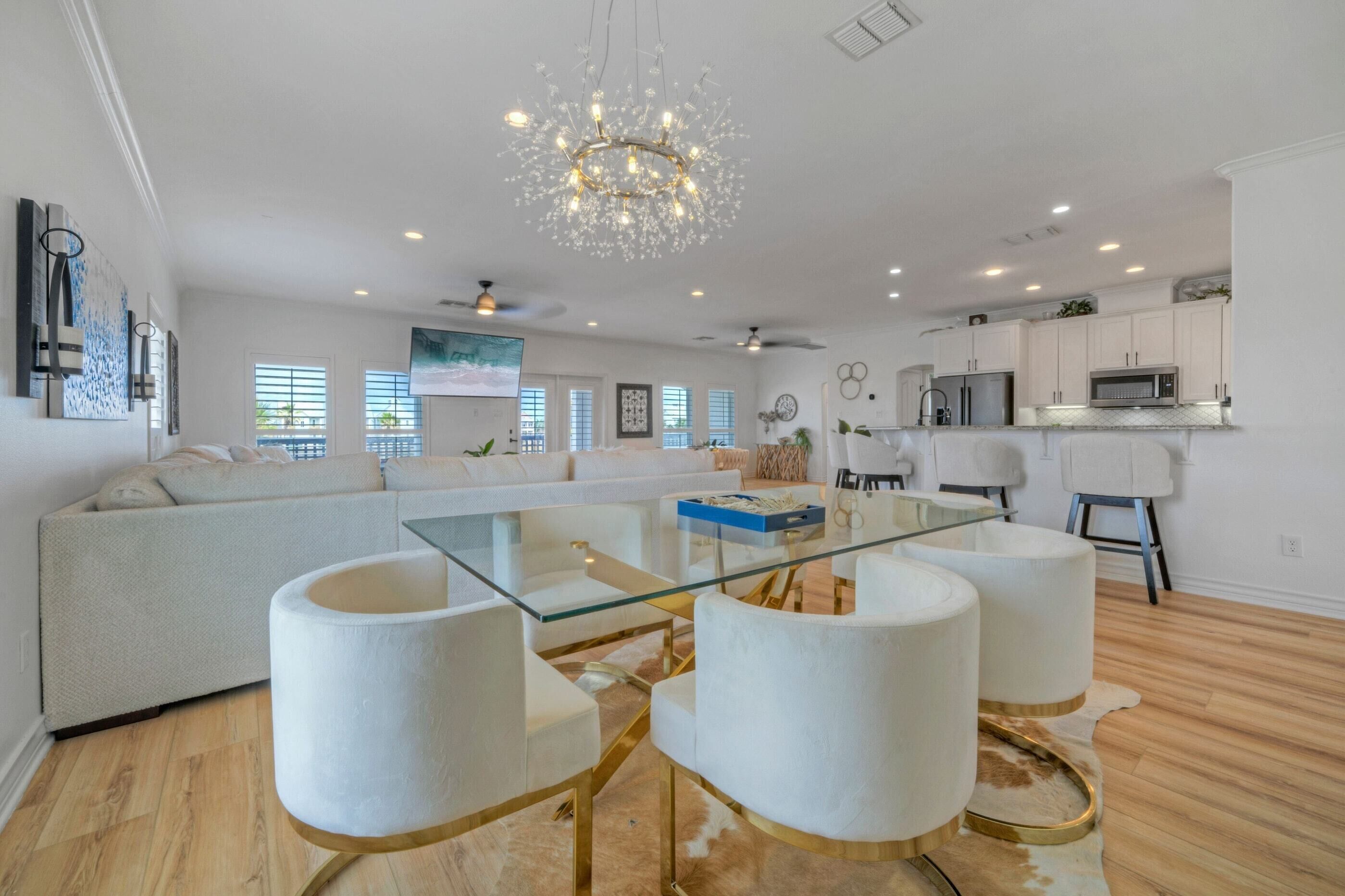 A modern living room with a glass coffee table, white sofas, and a chandelier.