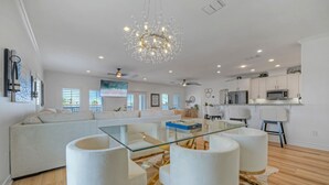 A modern living room with a glass coffee table, white sofas, and a chandelier. - Billiards & Beaches by Avantstay Cart Boardwalk + Pool Table (Port Aransas)
