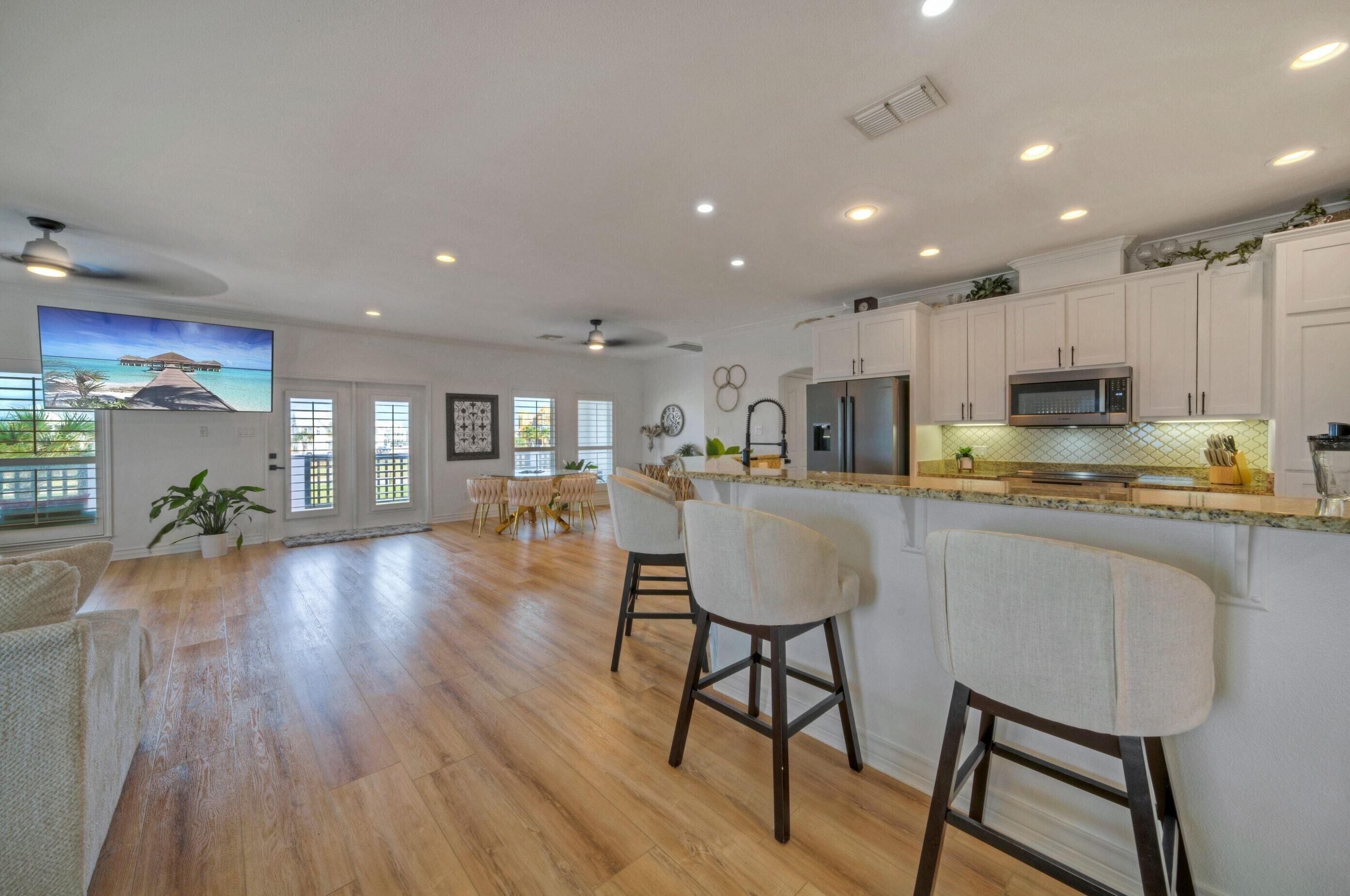 A spacious kitchen with white cabinets, a stainless steel refrigerator, and a large island with bar stools.