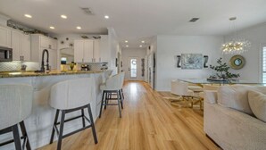 A modern kitchen with white cabinets, a stainless steel microwave, and a bar area with stools. - Billiards & Beaches by Avantstay Cart Boardwalk + Pool Table (Port Aransas)