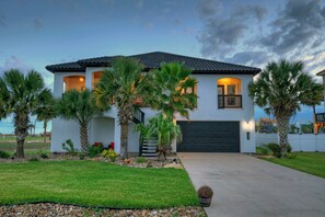 A two-story house with a dark garage door, surrounded by a well-maintained lawn and palm trees.