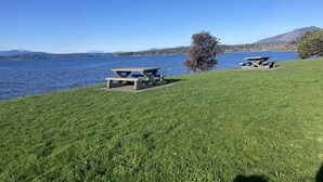 A grassy area with picnic tables by a lake, clear skies, and distant mountains. - Relaxing Country Retreat close to all amenities. Great for the whole family! (North Saanich)