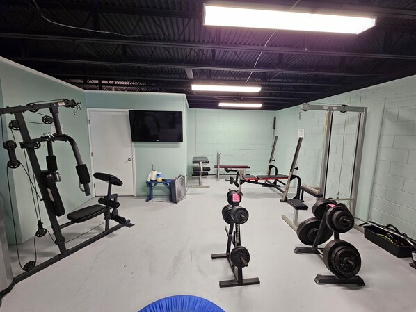 Une salle de sport équipée de divers appareils d’entraînement, notamment des machines de musculation, un banc et un ventilateur.