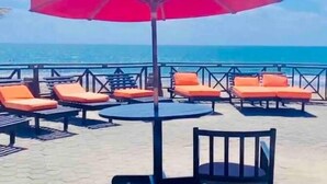 A beachside seating area with lounge chairs and a table, overlooking the ocean.