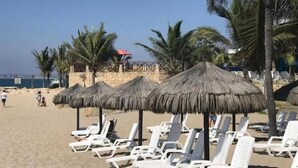 A beach with white lounge chairs, thatched umbrellas, and palm trees.