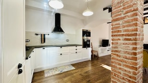A modern kitchen with white cabinets, a black range hood, and a brick accent wall.