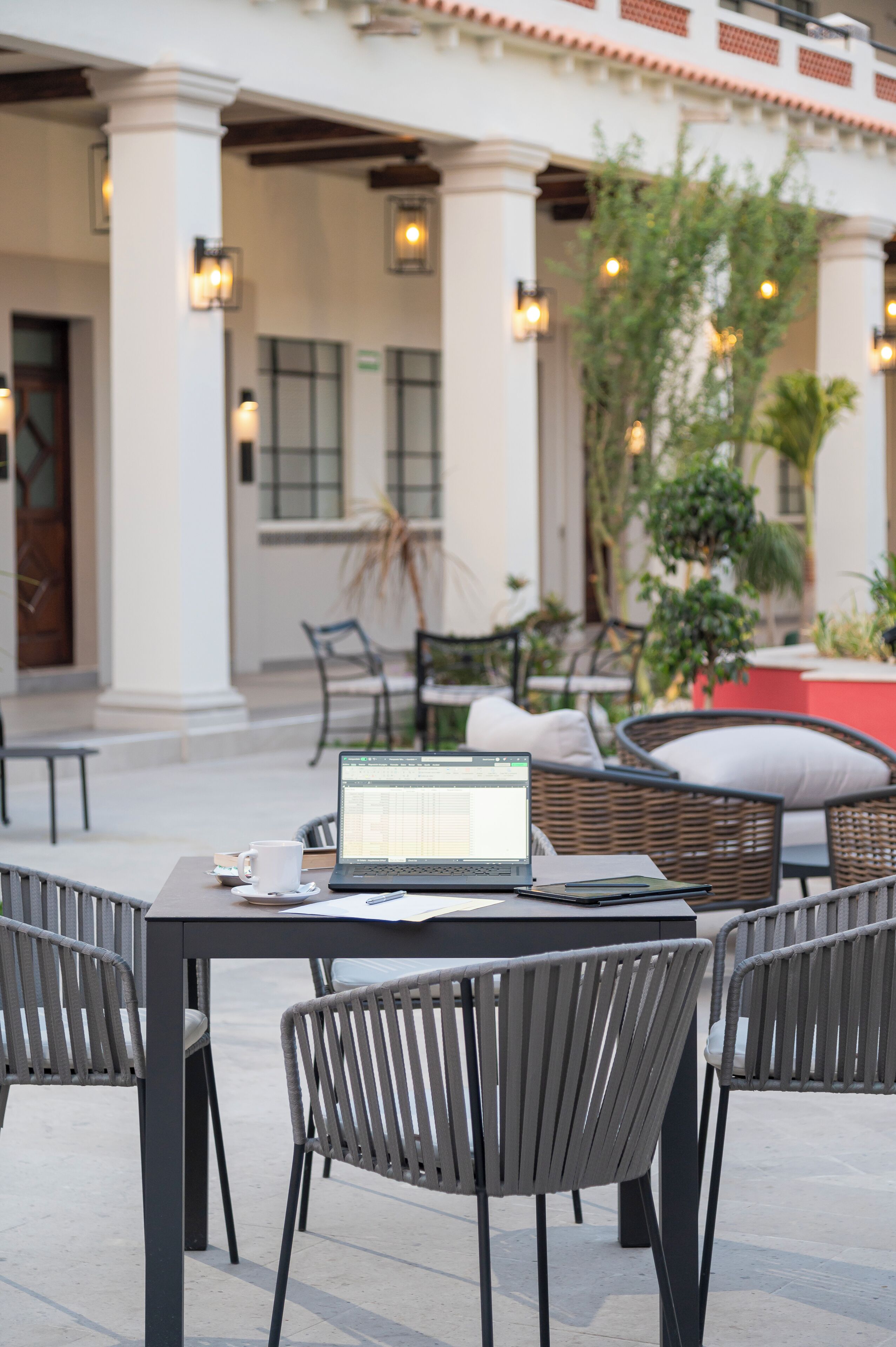 An outdoor seating area with a laptop on a table, surrounded by wicker chairs.