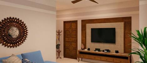 A living room with a blue sofa, a coffee table, a TV on a wooden stand, a ceiling fan, and a decorative wall piece.