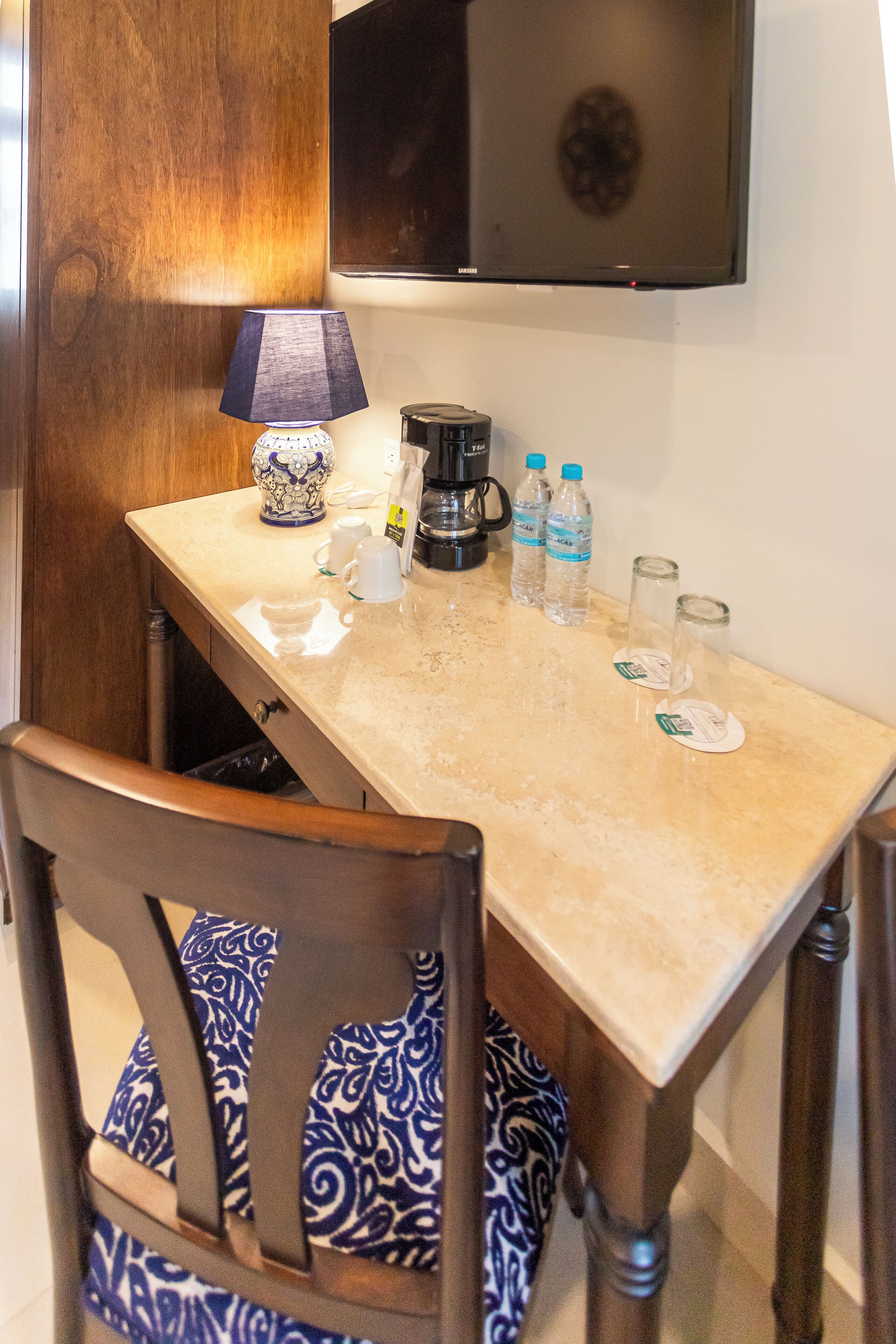 A dining area with a table, chairs, a lamp, a coffee maker, and water bottles.