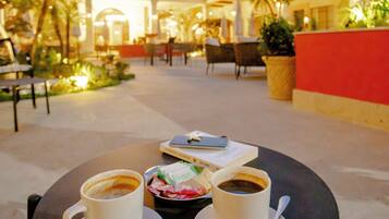 A table with two cups of coffee and a plate of pastries in an outdoor cafe setting.
