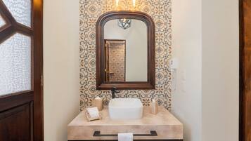 Une salle de bain avec un grand miroir, un lavabo blanc et un papier peint à motifs.