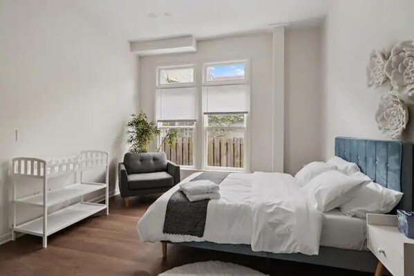 Une chambre à coucher avec un lit, une chaise, un berceau et une fenêtre avec des stores.