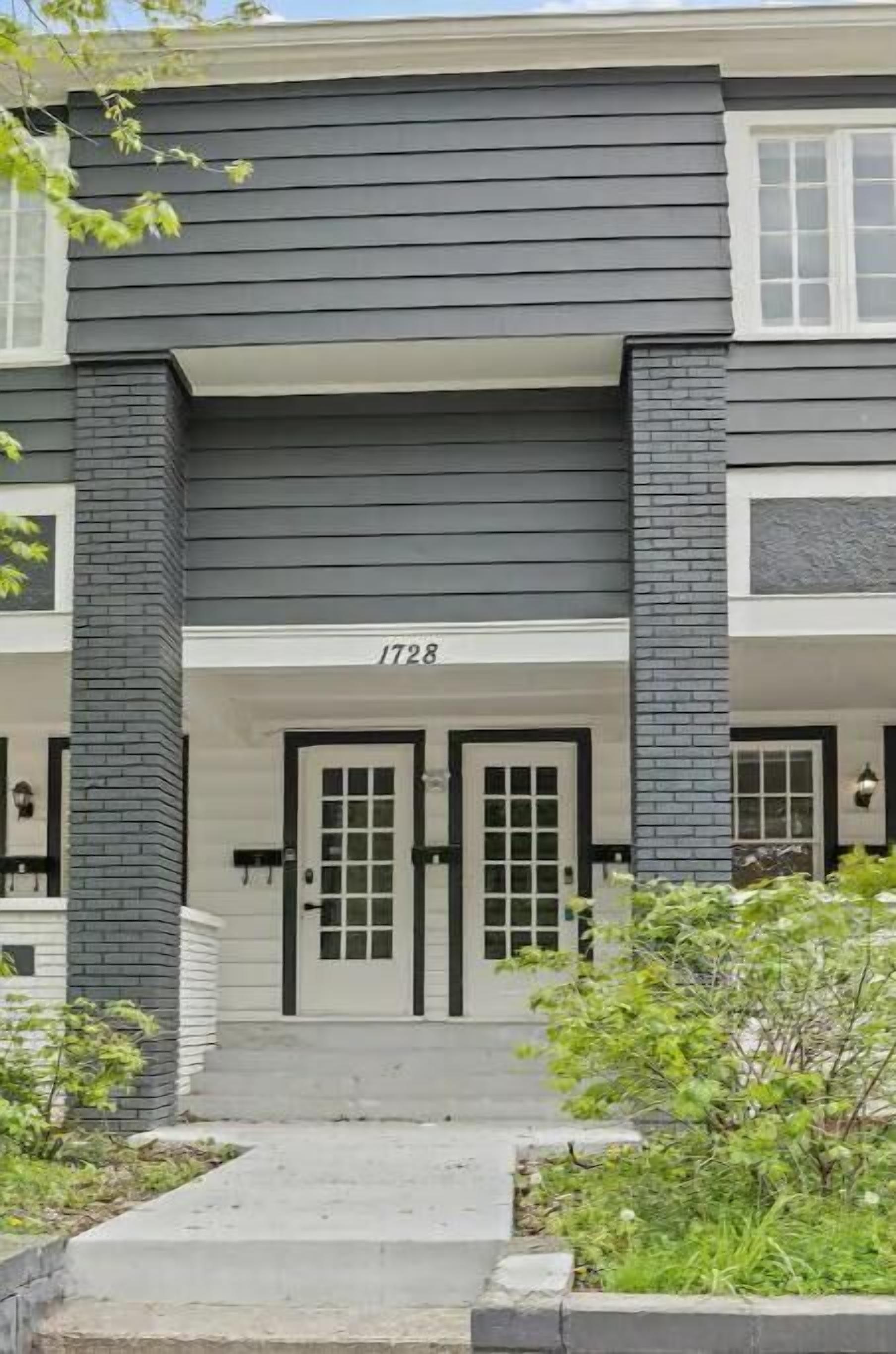 A two-story building with a dark gray exterior, white trim, and a number '1728' above the entrance.