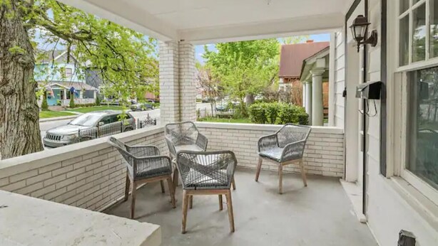 A covered porch with wicker chairs, a brick wall, and a view of the neighborhood. - Pink on Delaware, Spacious 2BR Downtown Indy (Indianapolis)