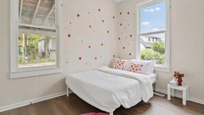 A bedroom with a bed, a window, and a small white nightstand with a vase of flowers. - Pink on Delaware, Spacious 2BR Downtown Indy (Indianapolis)