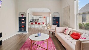 A spacious living room with a round coffee table, a sofa with red cushions, and a view to a kitchen and dining area. - Pink on Delaware, Spacious 2BR Downtown Indy (Indianapolis)